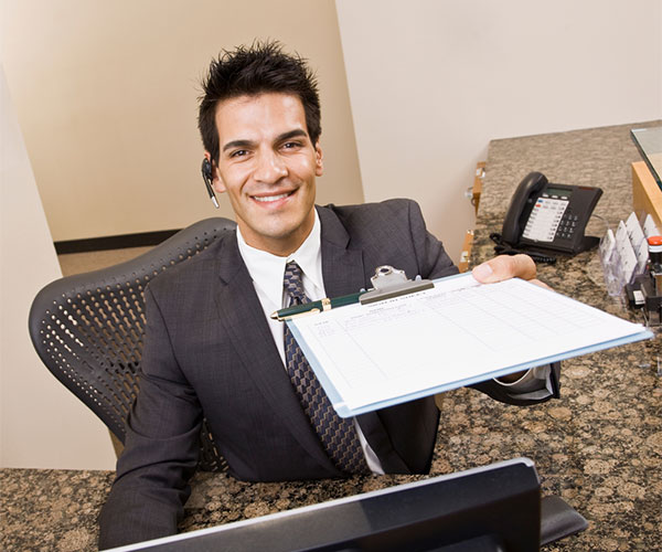 Man at reception desk handing a clipboard